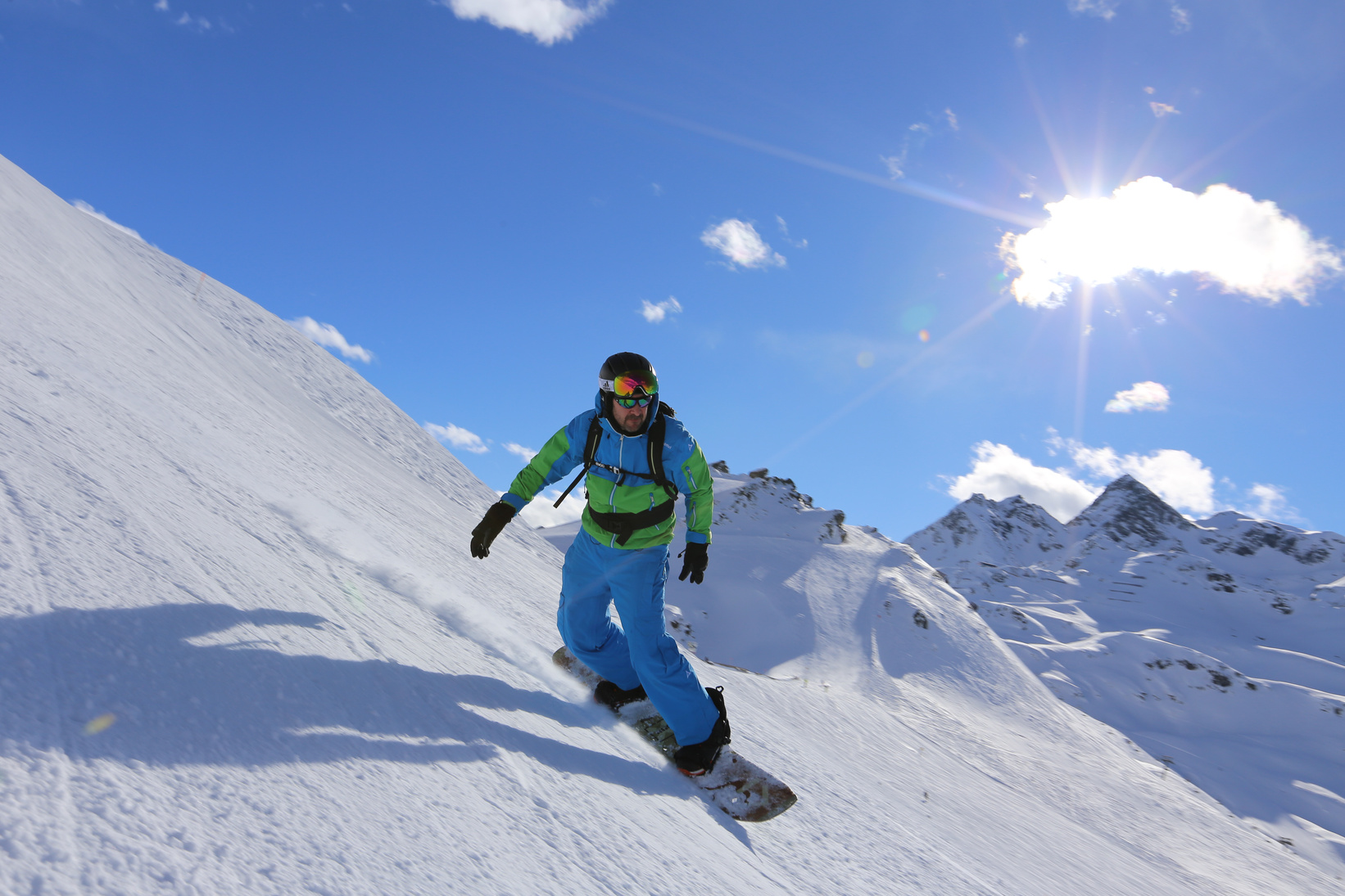 A Man in Green Jacket Snow Boarding under the Blue Sky